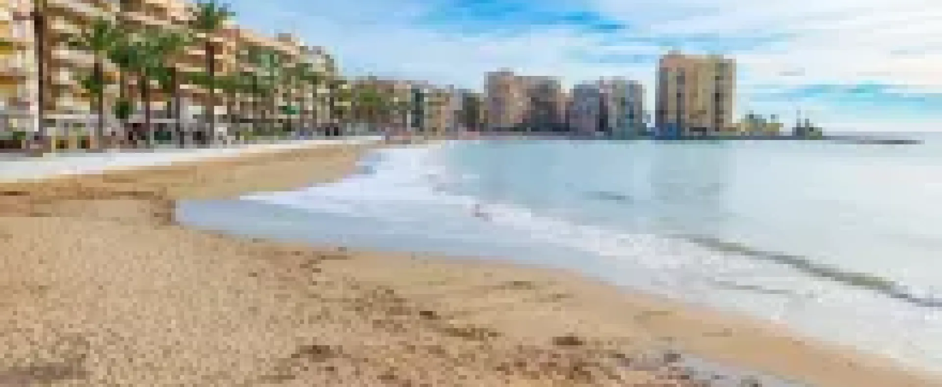 Vista de la Playa del Cura en Torrevieja, con turistas descansando en la arena, sombrillas, aguas tranquilas y el litoral al fondo.